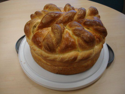 This image shows a traditional Ukrainian Easter bread, known as "paska," decorated with colorful, intricately woven designs made of dyed eggshells. The bread is a sweet, dense, and rich yeast bread that is typically made during the Easter season in Ukraine. The image highlights the cultural significance of Easter traditions in Ukraine, including the use of vibrant colors and intricate designs.